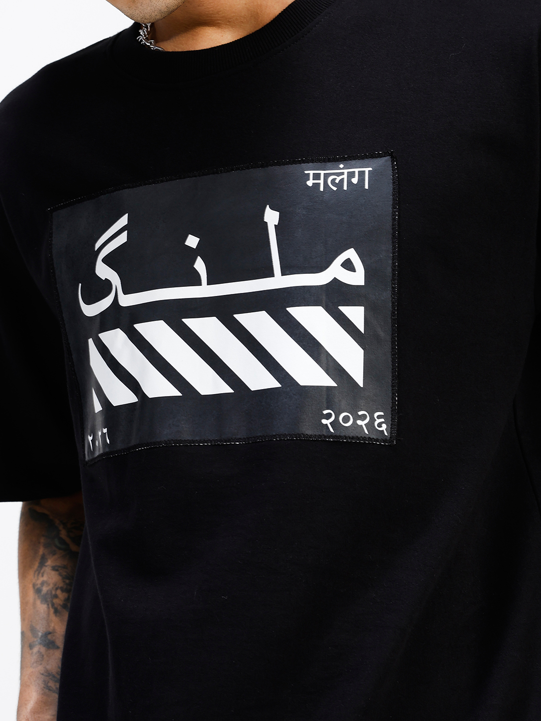 MALANG oversized black T-shirt front view showing Nastaliq calligraphy patch with diagonal stripes and Devanagari script