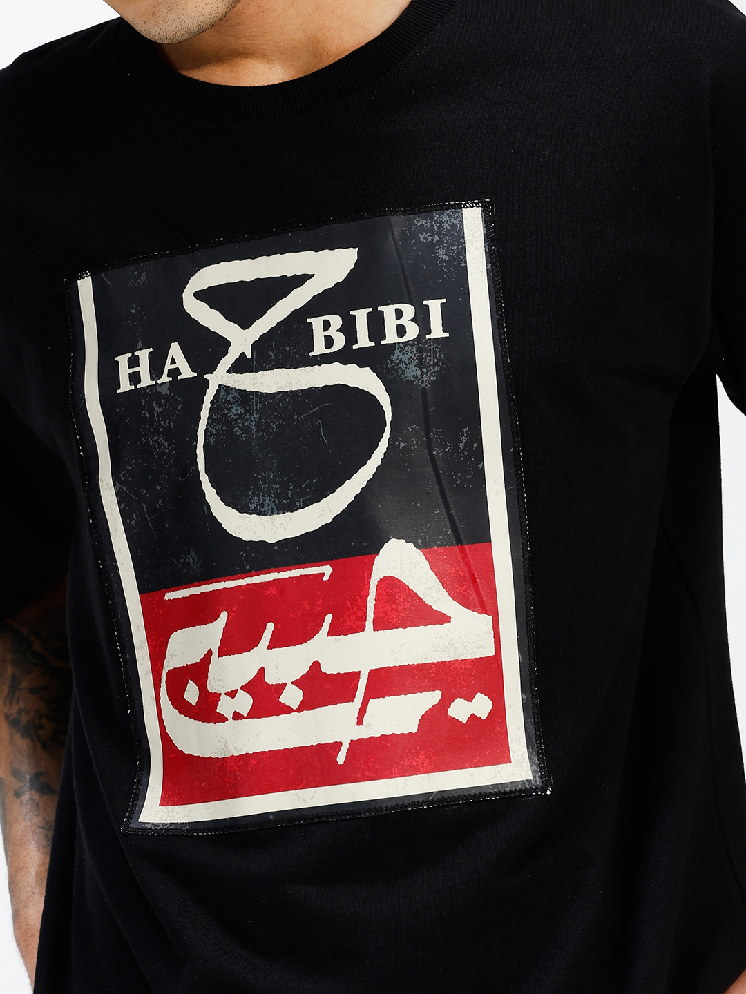 HABIBI oversized black T-shirt front view showing split black and red Nastaliq calligraphy patch with distressed finish